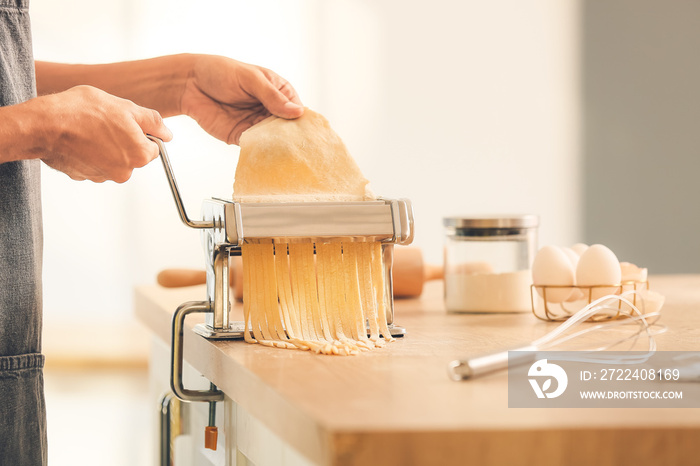 Man making pasta with machine on table in kitchen