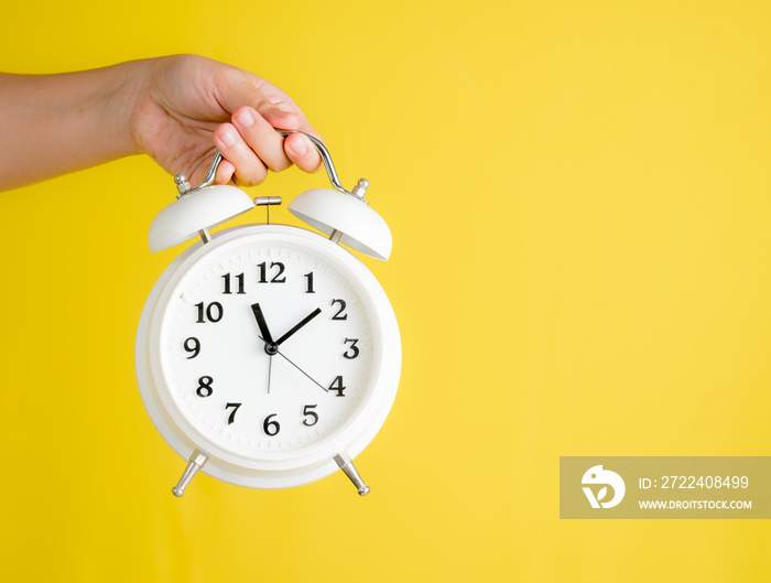 Hand holding white retro alarm clock with text space against yellow background