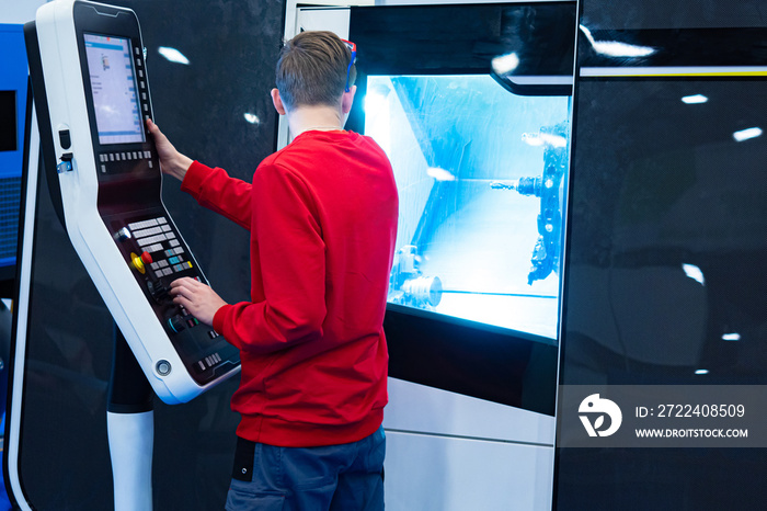 At the control panel is a man in a red sweater. The engineer programming the machine. The engineer monitors the operation of the unit. CNC machine. Adjustment of the conveyor line in production.