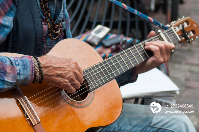 closeup of hands of old man playing on acoustic guitar in the street