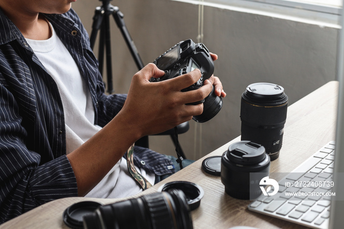 Young man photographer sitting and press button of professional camera to review shoot or setting camera at home office studio.