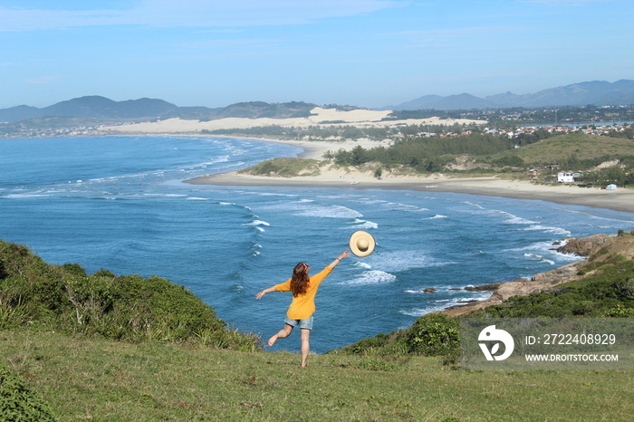 turista de roupa amarela em mirante de fente para o mar na Praia do Rosa, Santa Catarina