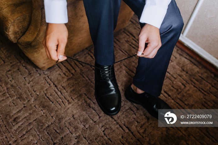 Man, groom, businessman tying shoelaces on black leather shiny shoes. Close-up photography, business.