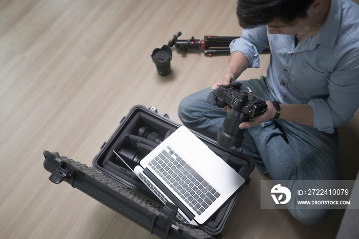 Professional photographer sitting on wooden floor and adjusts the camera.