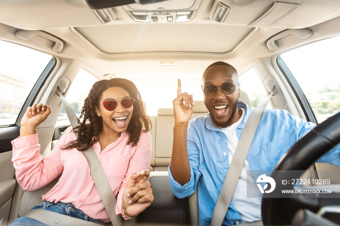 Excited black couple in sunglasses enjoying music driving luxury car