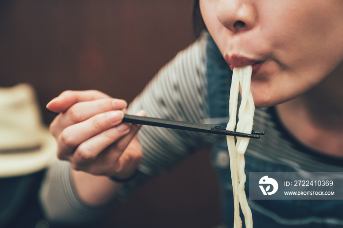 woman using chopsticks to clip noodles in mouth.