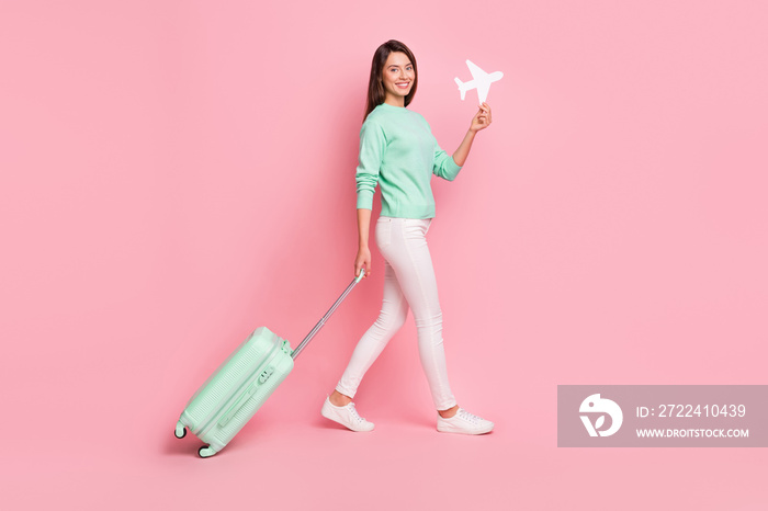 Full length body size profile side view of cheerful girl traveler going holding in hand paper plane isolated on pink color background