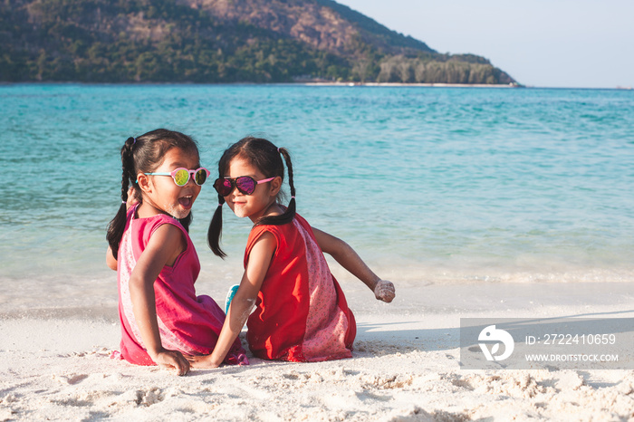 Two cute asian little child girls sitting and playing together on the beach near the beautiful sea in summer vacation