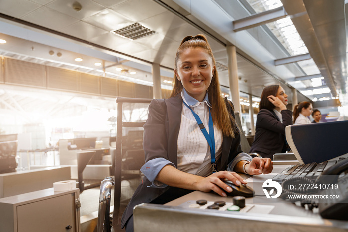 Woman airline employee working at airline check in counter in airport with colleagues on background