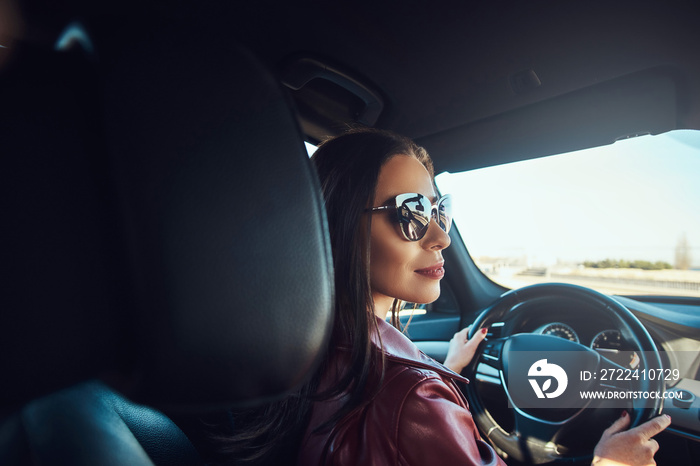 Attractive young woman in red jacket and sunglasses in driving her car.