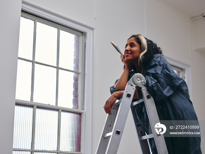 Smiling woman standing on ladder with paintbrush