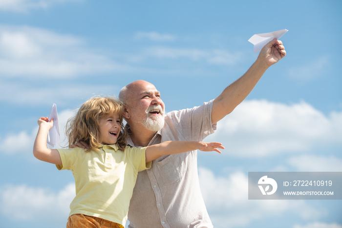 Young grandson and old grandfather with toy paper plane against summer sky background. Child boy with dreams of flying.