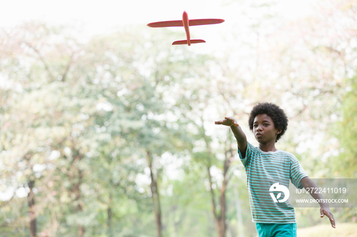 African American boy playing with toy airplane outdoor. Kid having fun with toy airplane in the park. Happy black people. Education and field trips concept