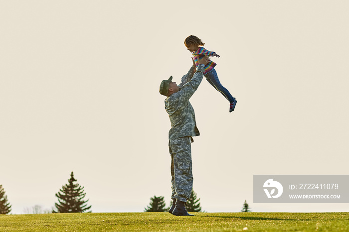 Soldier lifting up little kid. Father in military uniform is playing with daughter in the park.