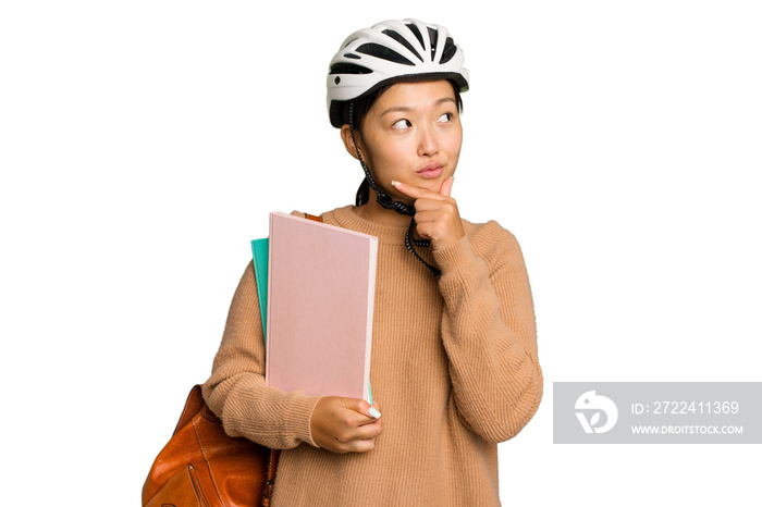 Young student asian woman wearing a bike helmet isolated on green chroma background looking sideways with doubtful and skeptical expression.