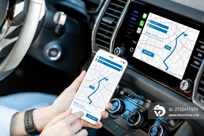 Close-up of a smartphone with navigation app in the modern car with monitor on the background