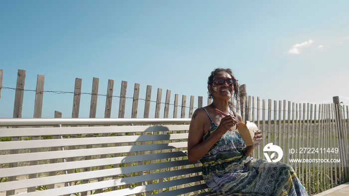 Senior woman sitting on bench and eating take out food