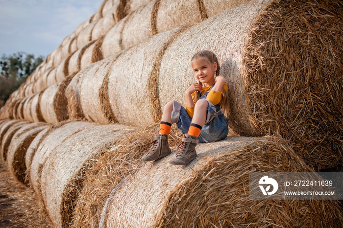 Cute girl having fun on rolls of hay bales in field