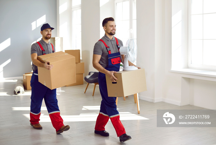 Two workers from moving company or truck delivery service removing belongings from house or apartment. Happy young Caucasian men in workwear uniforms carrying cardboard boxes and other things