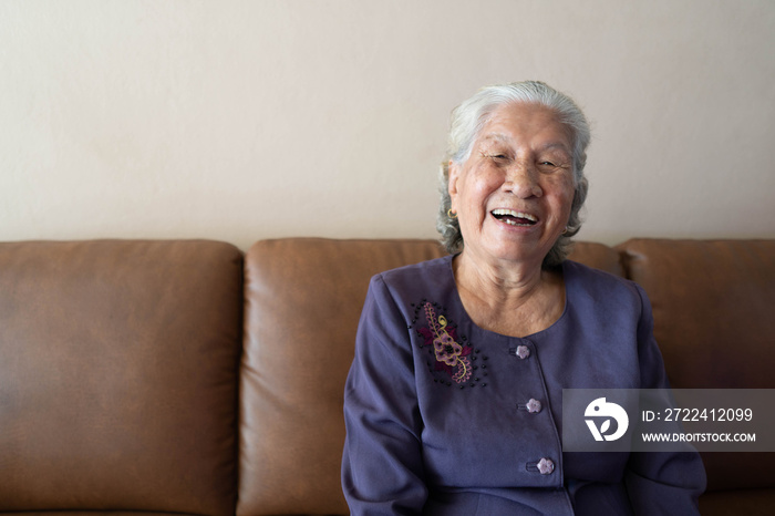 Happy senior asian woman smiling and laughing while sitting on a couch at home. Healthy living for the elderly concept.