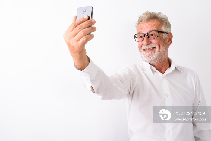 Studio shot of happy senior bearded man smiling while taking sel