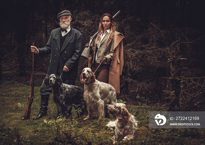 Two hunters with dogs and shotguns in a traditional shooting clothing.