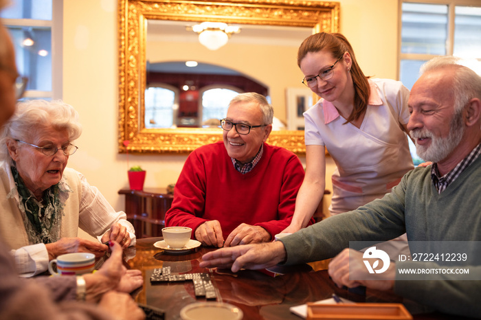 Nurse serving tea while older people play board games