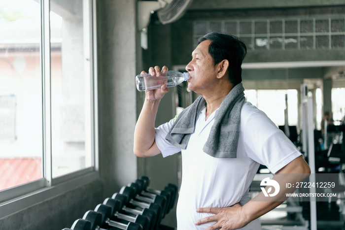 asian senior man thirsty drinking water after exercise in fitness gym. elderly healthy lifestyle.