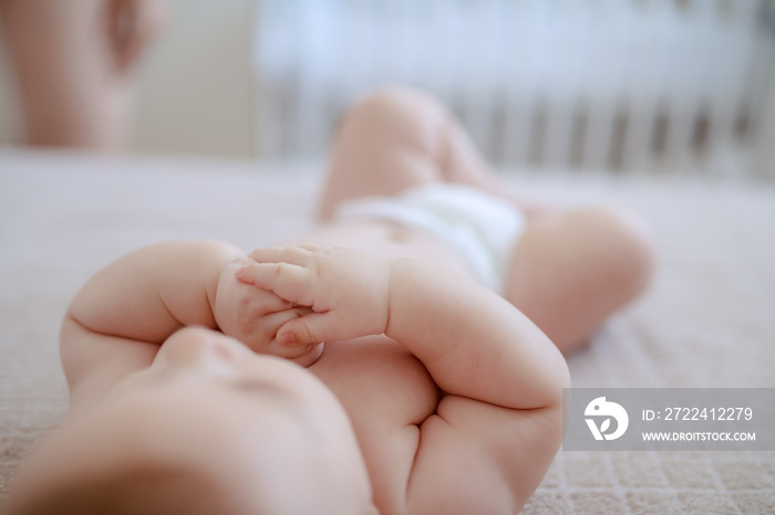 6 months old baby boy lying on bed in diaper. Baby putting fingers in mouth. Selective focus on hands.