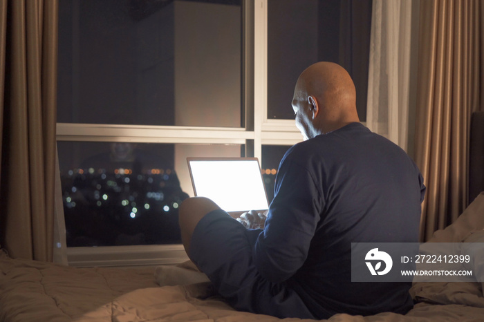 Happy smiling business, black man, African American people working from home and using computer notebook laptop with blank screen in quarantine on bed in bedroom at home at late night. Lifestyle