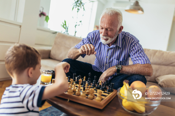 Young boy is playing chess with his grandfather at home.