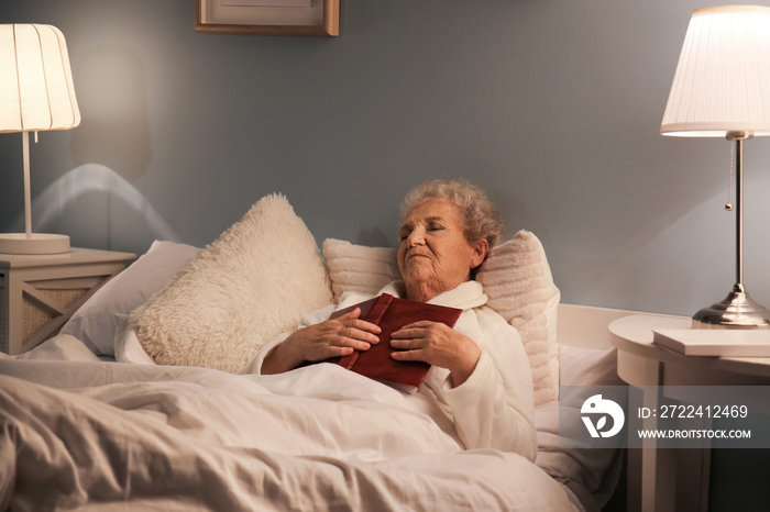 Senior woman with book sleeping in bed at night