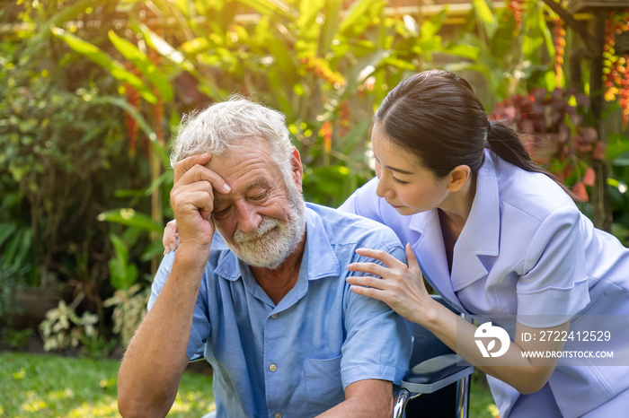 Nurse take care and comfort depressed thoughtful elderly man on wheelchair in garden at nursing home