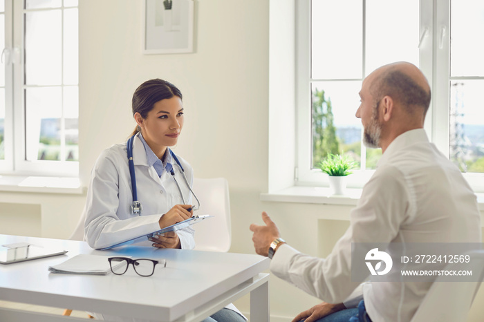 Male patient pensioner speaks with the doctor at the desk in the office of the hospital.