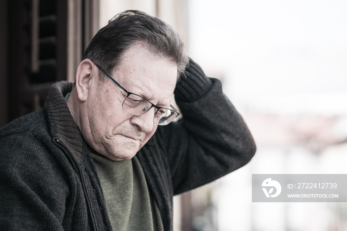 dramatic portrait of sad and depressed mature man 65 - 70 years old at home balcony lonely and confused facing getting old and retirement alone looking away