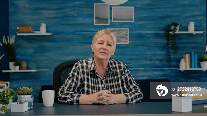 POV of elderly aged woman waving during a video conference with business partners working from home. Senior person using internet online chat technology webcam making virtual meeting call connection