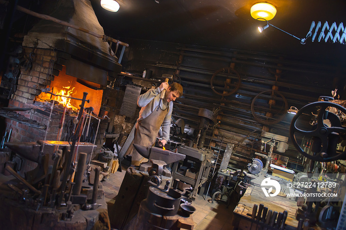 The blacksmith manually forging the red-hot metal on the anvil in smithy with spark fireworks