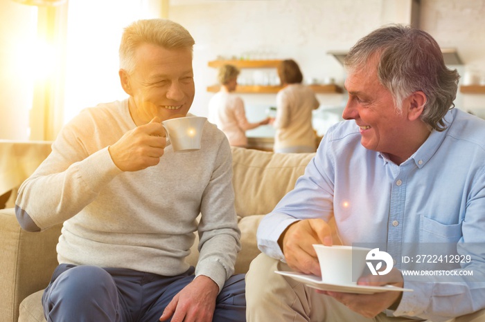 Smiling mature men holding coffee while sitting on sofa at home