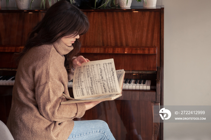 Young woman musician looks into a collection of notes, sitting at the piano.