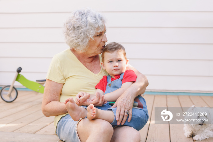 Grandmother sitting with grandson boy on porch at home backyard. Bonding of relatives and generation communication. Old woman with baby having fun spending time together outdoors.