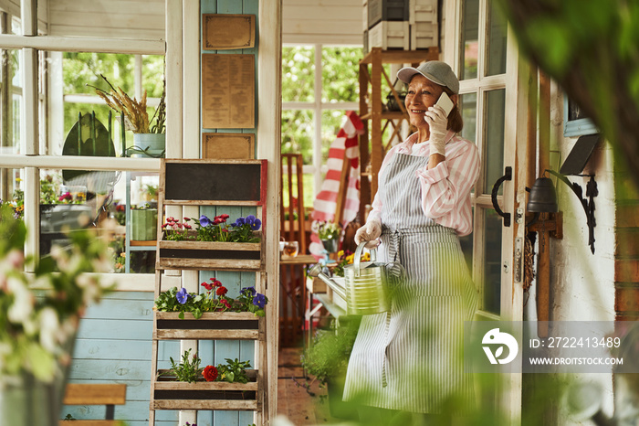 Cheerful female with watering can speaking on smartphone