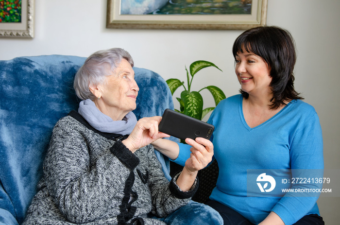 Cheerful female caregiver teaching an elderly woman how to use a smartphone