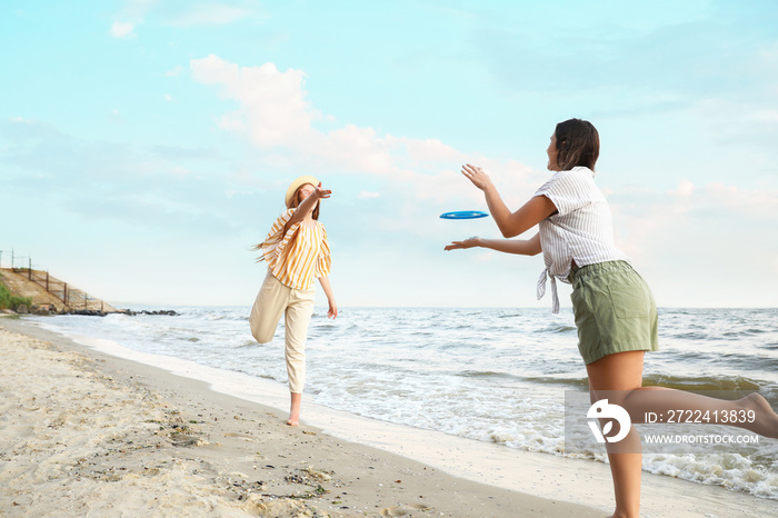 Happy young women playing frisbee on sea beach