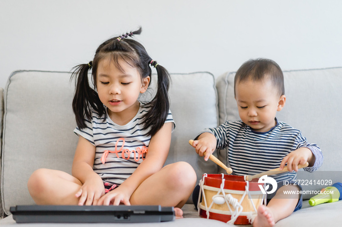 Little sister and her baby brother play with keyboard and drum and singing.Asian child playing and singing happy moment in music time.Sibling child sing in music song class at home.