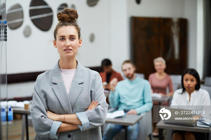 Waist up portrait of contemporary young woman looking at camera confidently with group of students in background, copy space