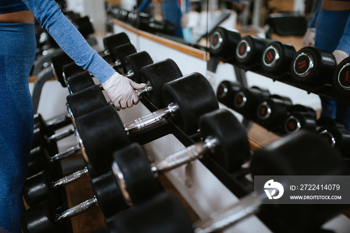 Close up of hands of girl with gloves while lifting weights in the gym. COVID - 19 virus protection