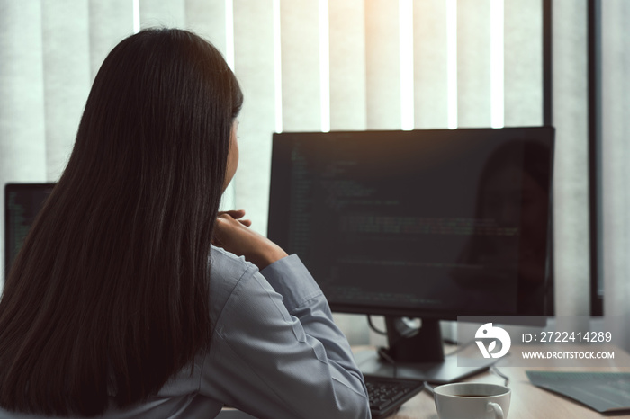 Asian woman software developers sitting in front of computers looking at computer codes on the screen.