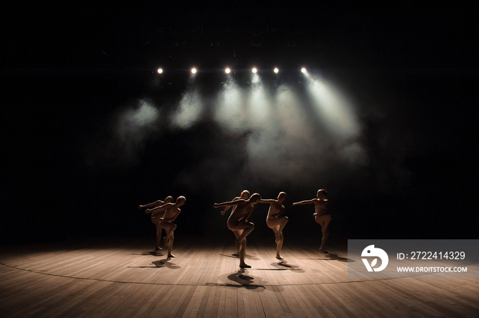 A group of small ballet dancers rehearses on stage with light and smoke