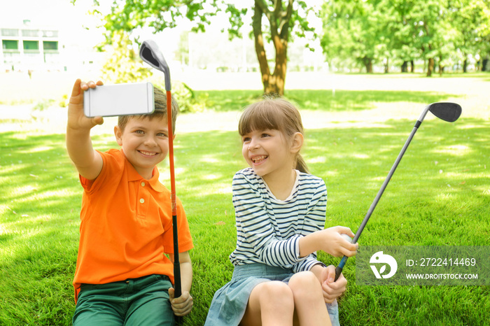 Cute children taking selfie while sitting on golf course in sunny day