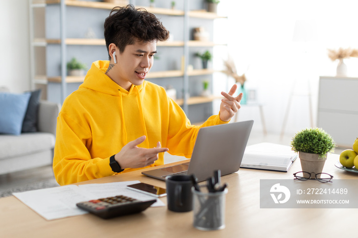 Asian man using laptop wearing headphones sitting at desk